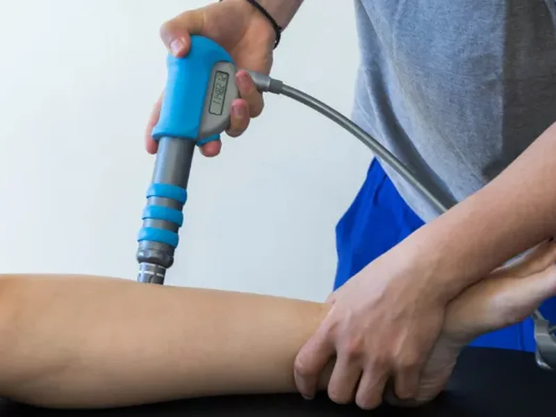 Doctor of Physical Therapy administering shockwave therapy on a patient's forearm
